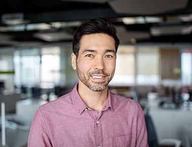 Close-up portrait of Asian mature businessman in the office. Japanese business executive with light beard smiling at the camera.