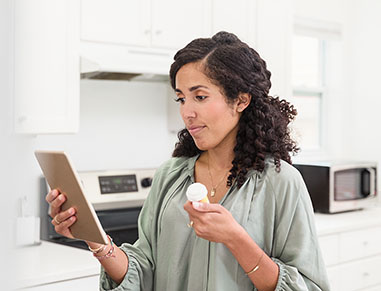 A woman talks with her doctor during a telemedicine appointment. The woman is holding a pill bottle while talking with the doctor about a prescription medication.